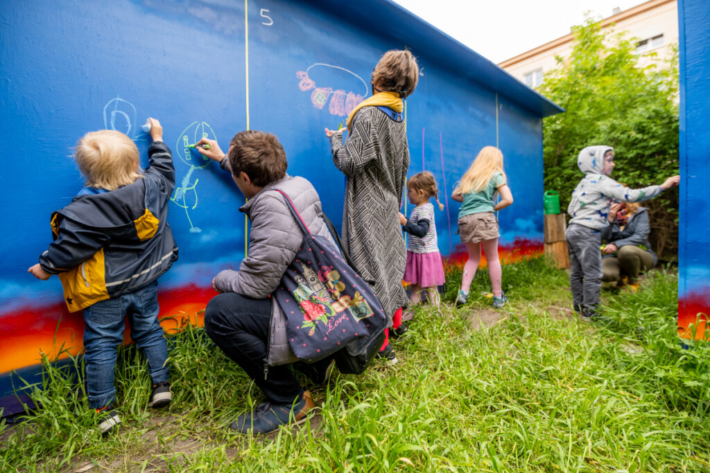 Dzieci i dorośli malują po ścianach budynku.