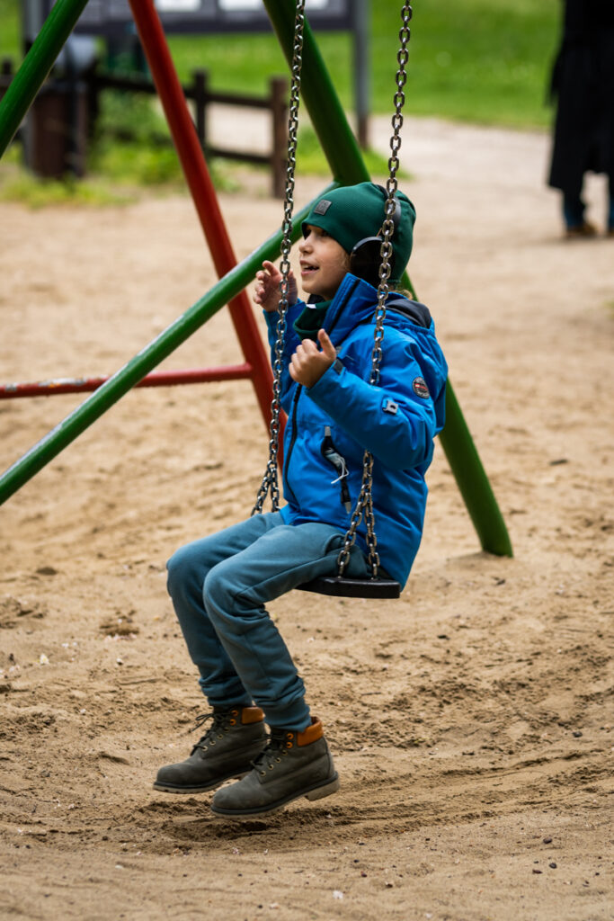 Uśmiechnięte dziecko siedzi na huśtawce, na uszach ma słuchawki.