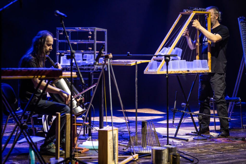 Koncert. Na scenie dwoje mężczyzn gra na niekonwencjonalnych instrumentach.