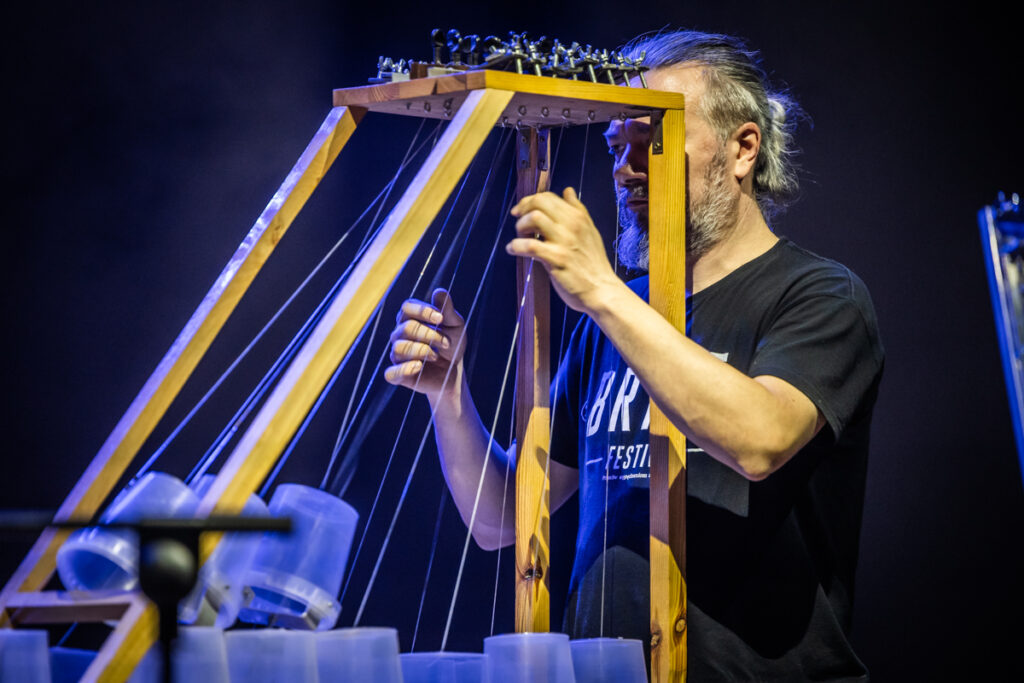Koncert. Mężczyzna z brodą szarpie struny ogromnego, tajemniczego instrumentu.