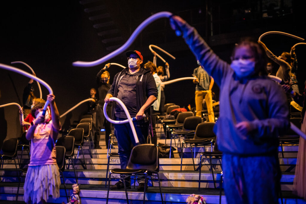 Grupa dzieci i dorosłych z widowni bawi się przy użyciu giętkich rur.