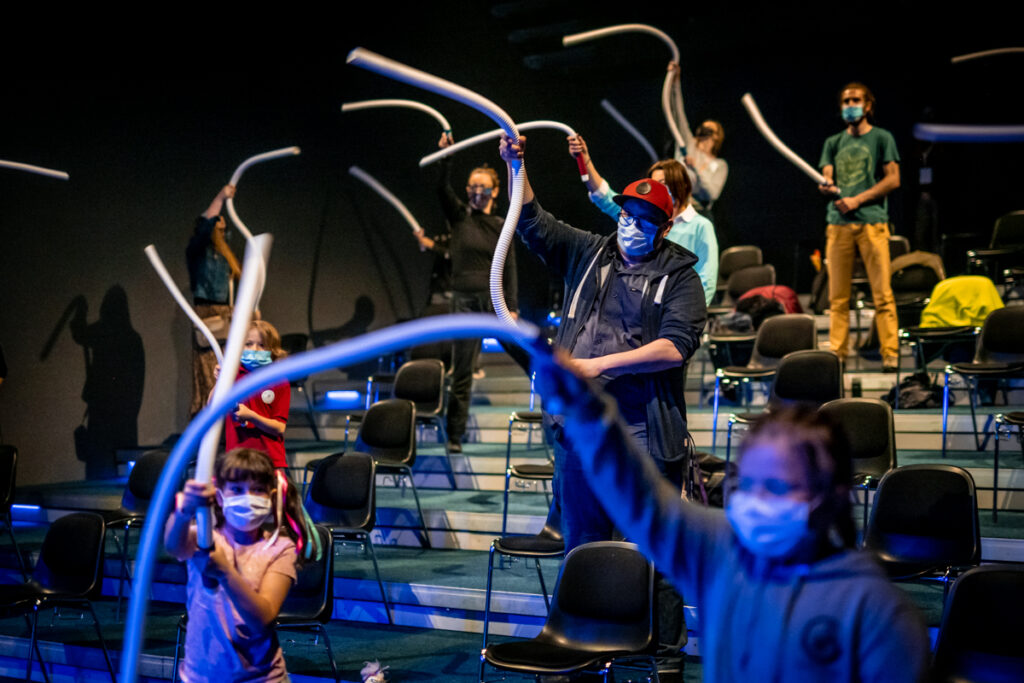 Grupa dzieci i dorosłych z widowni bawi się przy użyciu giętkich rur.