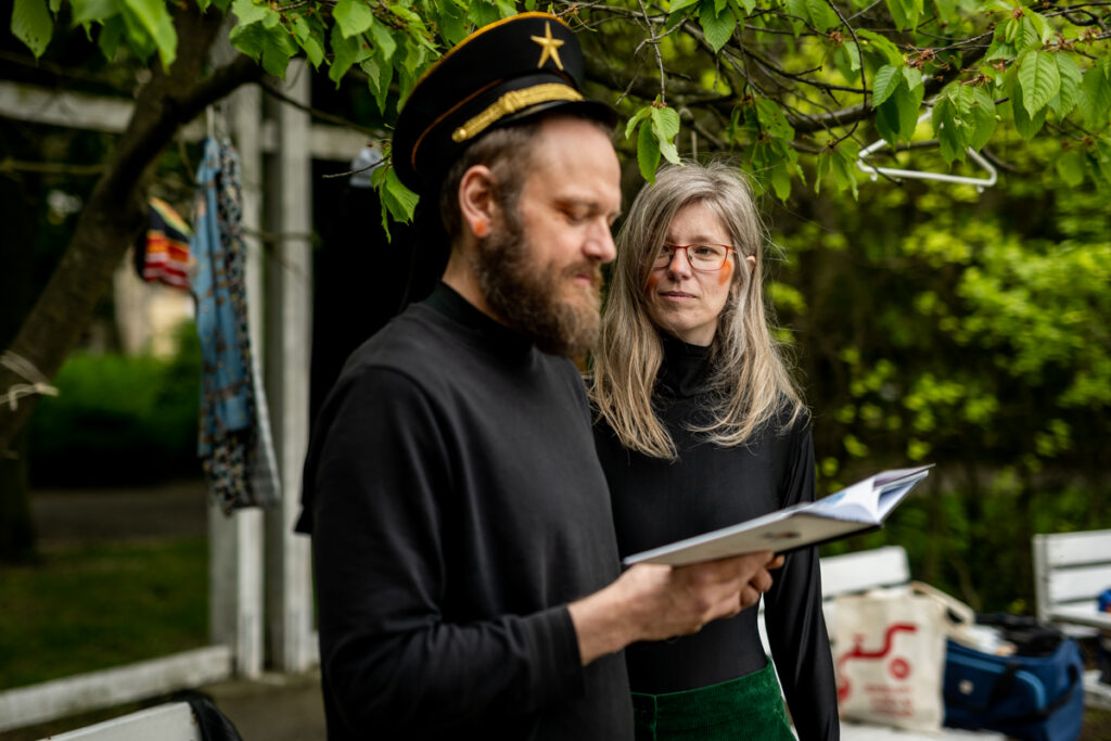 Park. Mężczyzna czyta książkę. Za nim stoi kobieta w okularach.