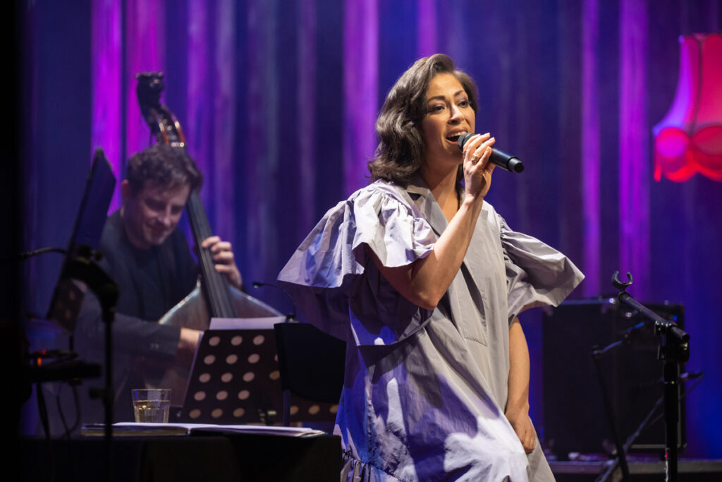 Kobieta śpiewa do mikrofonu. W tle mężczyzna grający na kontrabasie.