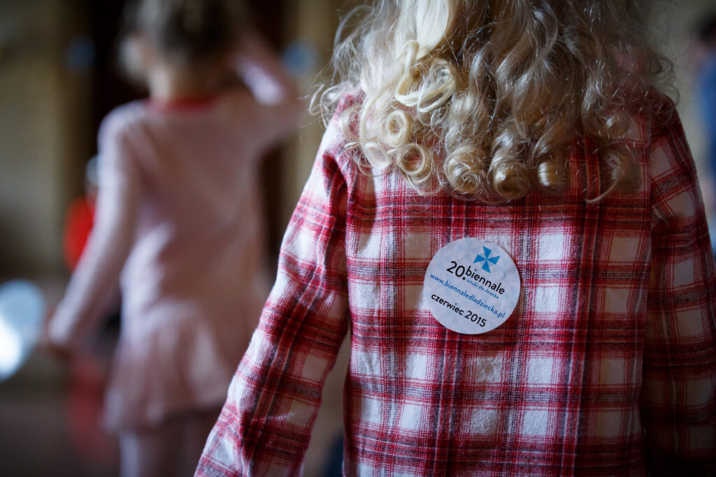 Na zdjęciu plecy dziecka, a na nich plakietka z napisem: 