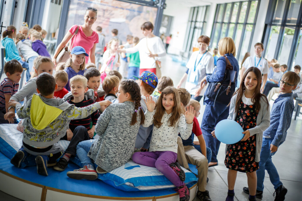 Na zdjęciu tłum dzieci i rodziców w foyer Sceny Wspólnej. Niektórzy uśmiechają się patrząc w obiektyw