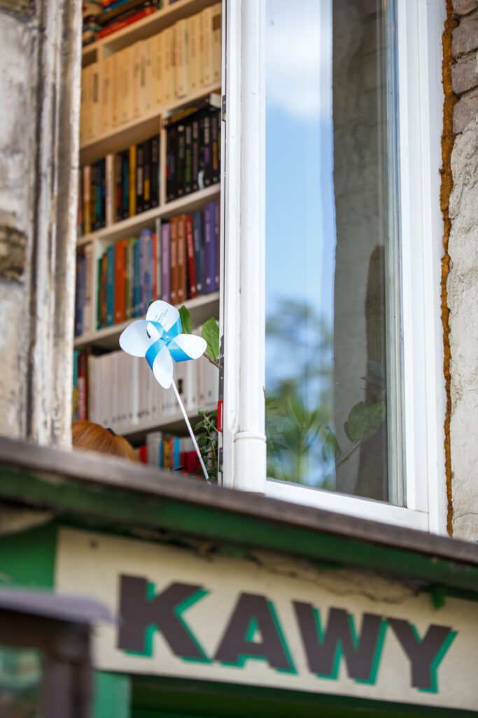 Na zdjęciu widoczny od zewnątrz przez okno niebieski wiatraczek Biennale.