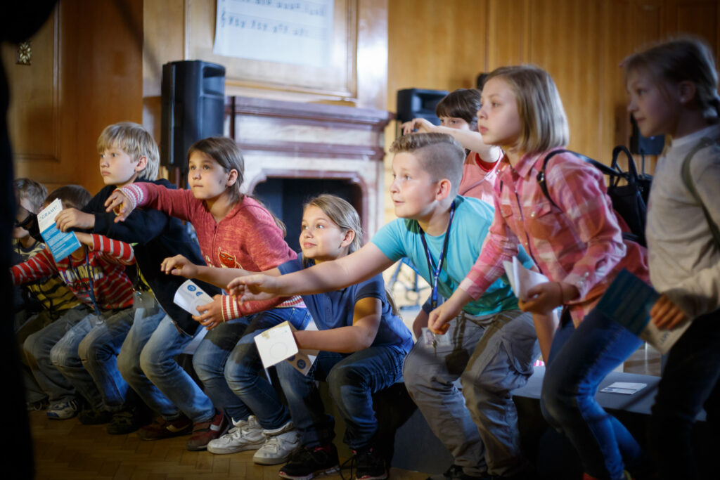 Na zdjęciu rząd dzieci, które kucają.