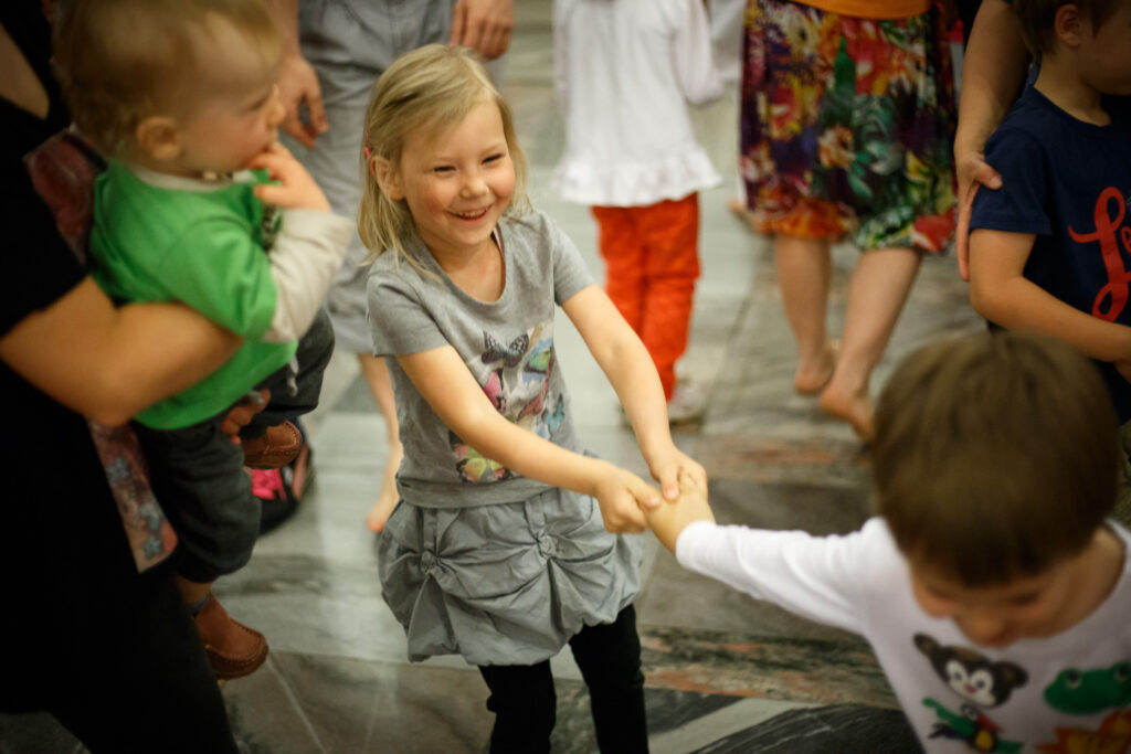 Na zdjęciu tańczące dzieci. Dziewczynka trzyma chłopca za rączkę i szeroko się śmieje