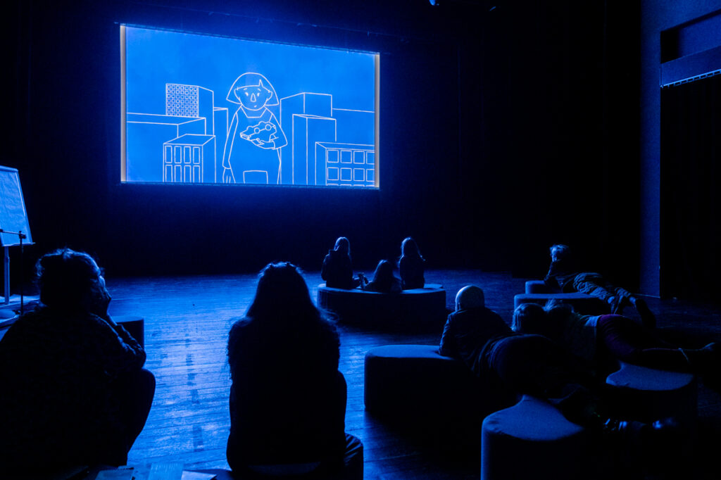 Osoby oglądają film wyświetlany na dużym ekranie.