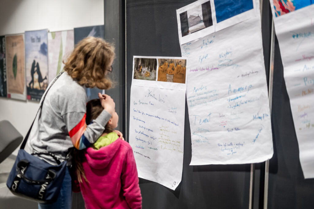 Dwie dziewczynki oglądają plakat zawieszony na ścianie.