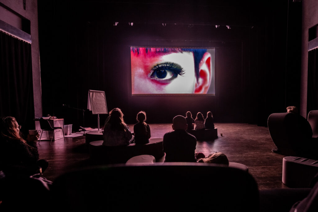 Osoby oglądają film wyświetlany na dużym ekranie.