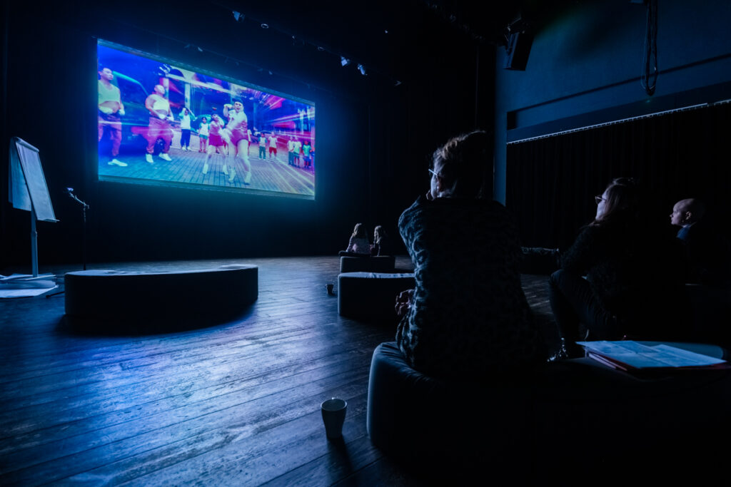 Osoby oglądają film wyświetlany na dużym ekranie.