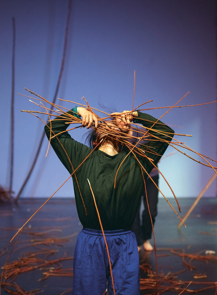 Kobieta trzyma nad głową kilkanaście witek wierzbowych. Witki zasłaniają jej twarz.