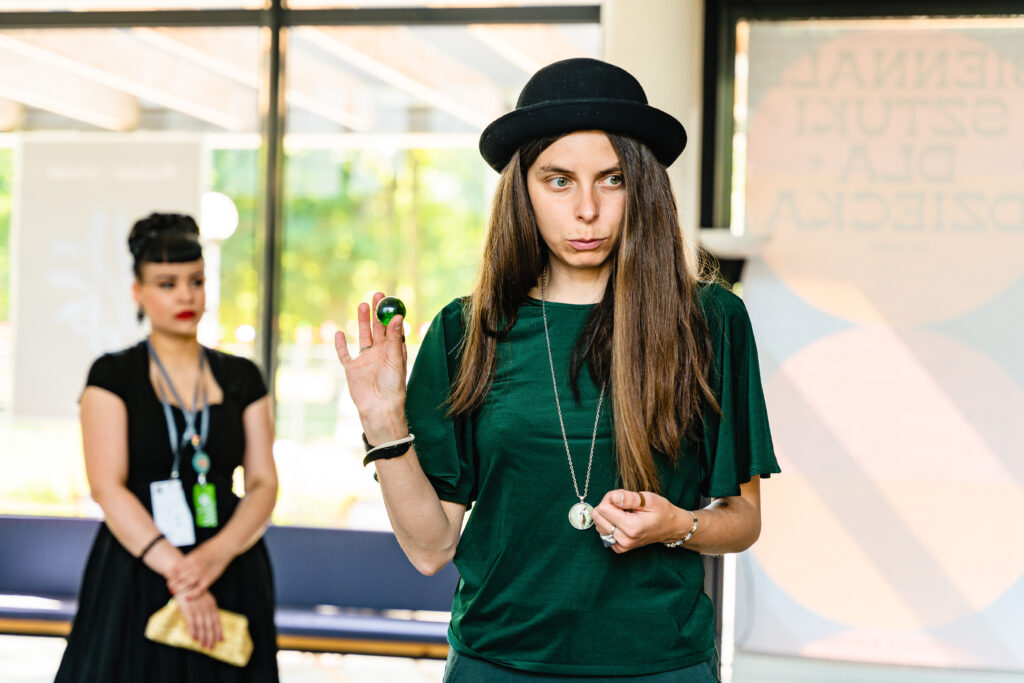 Kobieta w kapeluszu trzyma w ręku zieloną kulkę.