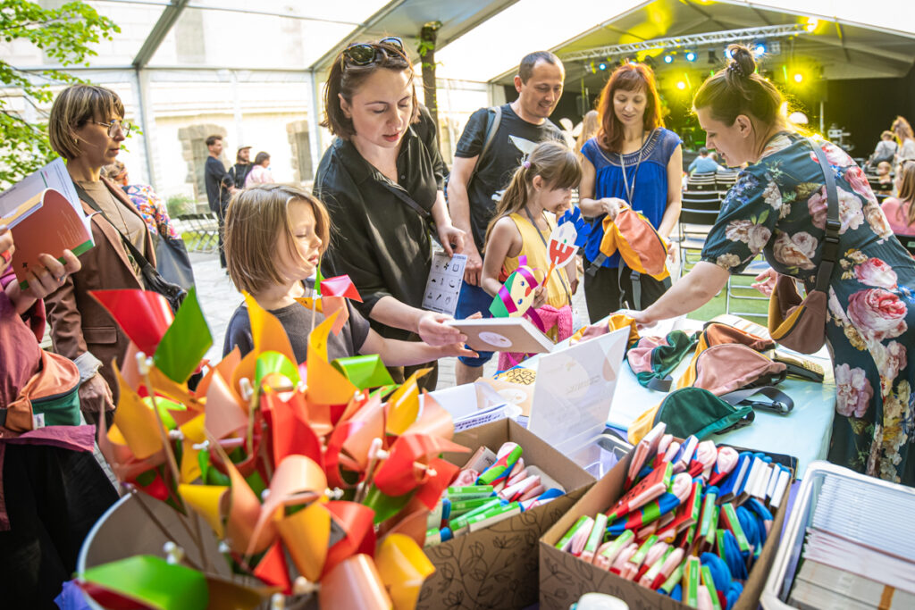 Grupa dzieci i dorosłych przed stoiskiem z materiałami promocyjnymi Biennale Sztuki dla Dziecka.