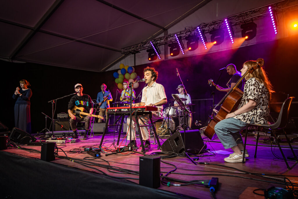 Na scenie grupa muzyków. W środku mężczyzna gra na klawiszach i śpiewa.
