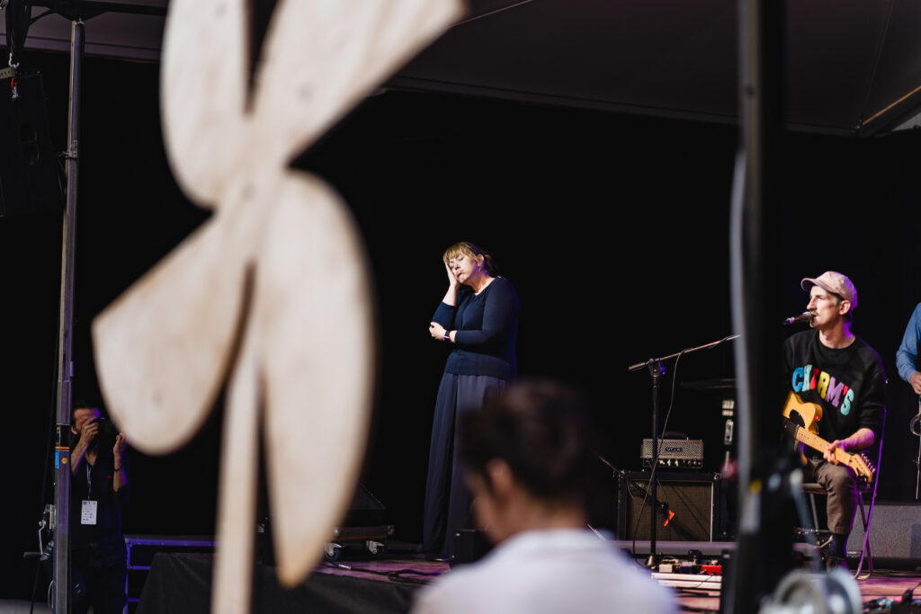 Po prawej muzyk z gitarą śpiewa. Obok niego kobieta używająca języka migowego.