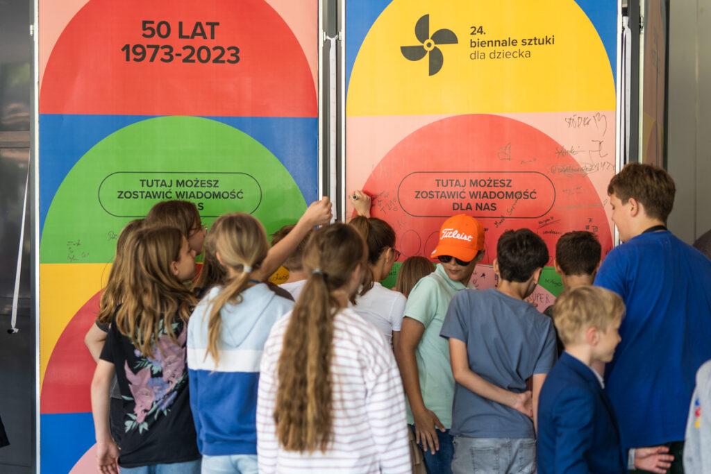 Grupa dzieci soi przed tablicą z napisem: Tutaj możesz zostawić wiadomość dla nas.