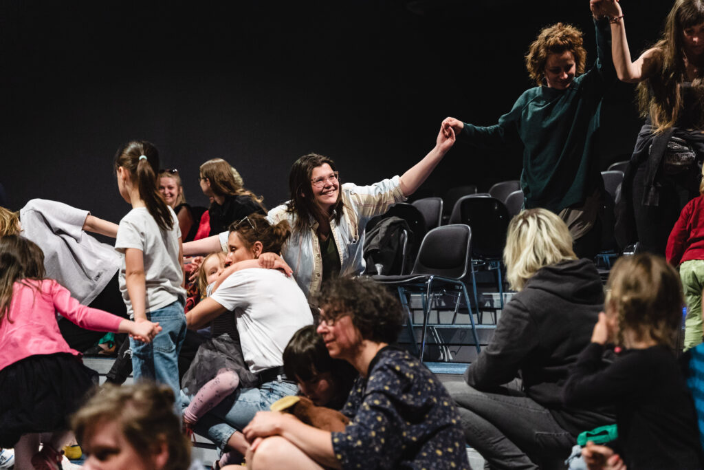 Na widowni grupa osób. Kilkoro trzyma się za ręce.