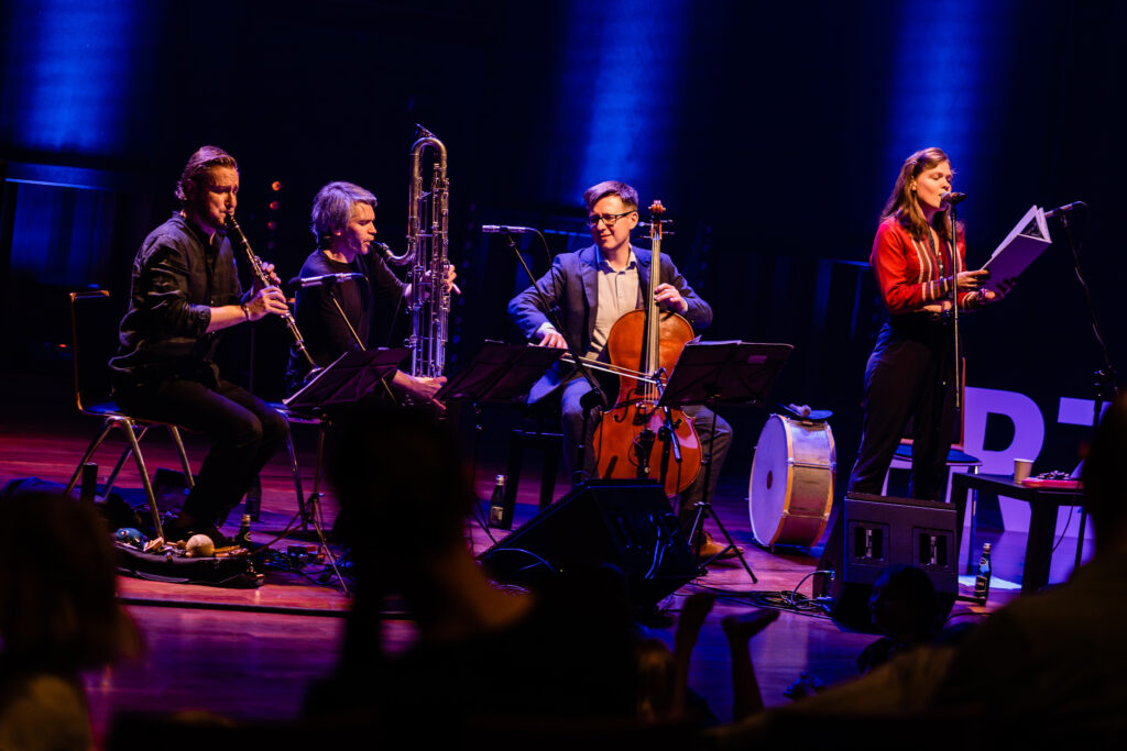 Trójka muzyków gra na instrumentach muzycznych. Po prawej piosenkarka śpiewa.