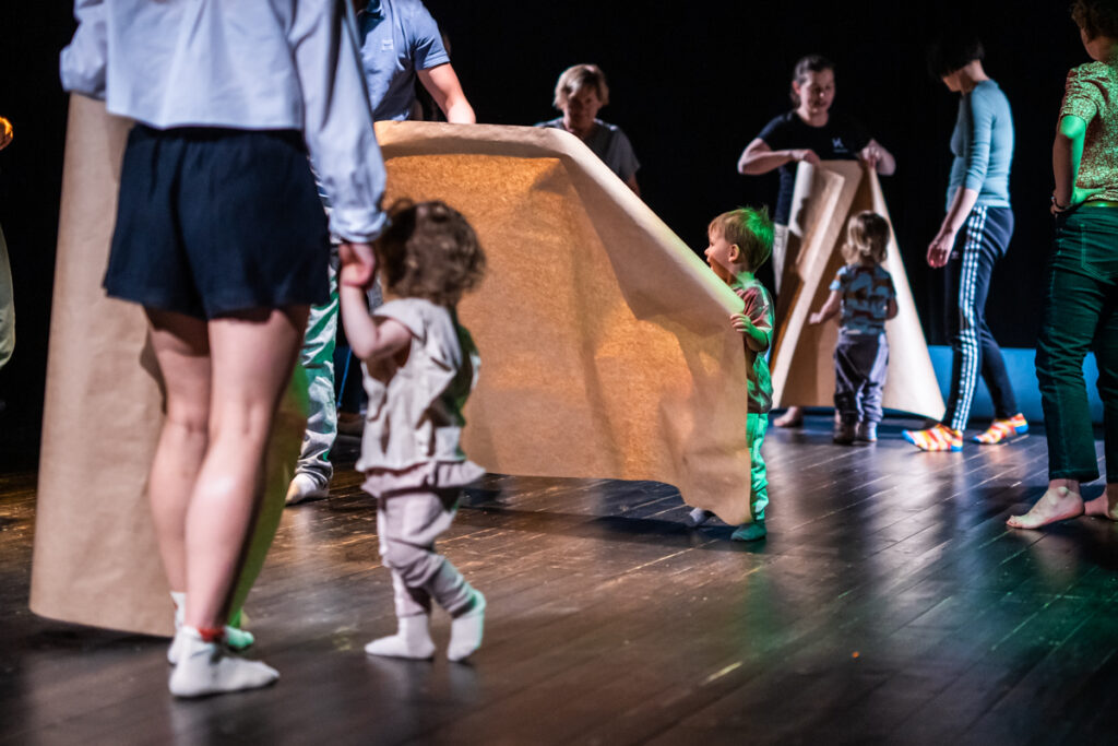 Na scenie grupa dzieci i dorosłych trzyma w rękach duże kawałki papieru.