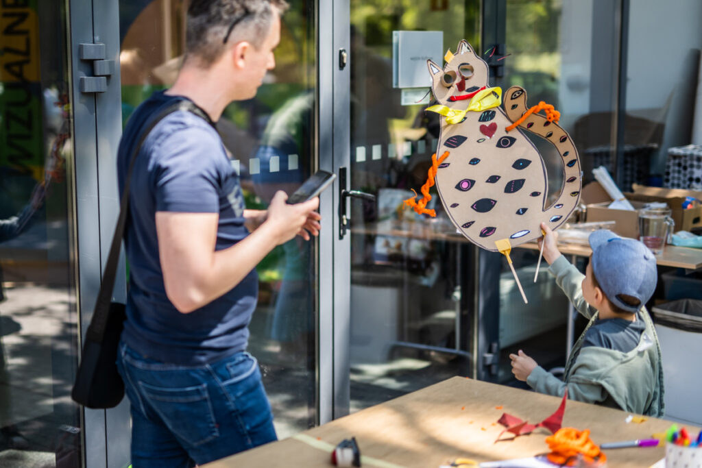 Chłopiec unosi w górę kartonowego kota, pokazuje go stojącemu obok mężczyźnie.