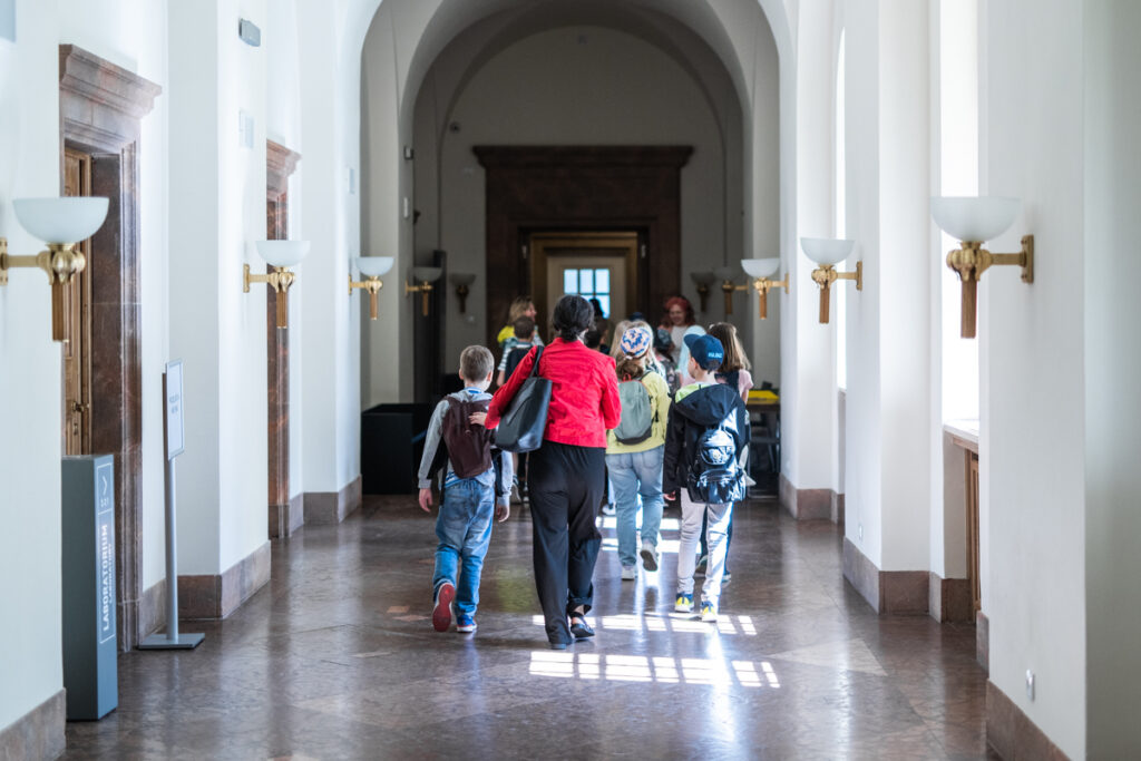 Korytarz w poznańskim Zamku. Grupa dzieci i dorosłych idzie widziana od tyłu.