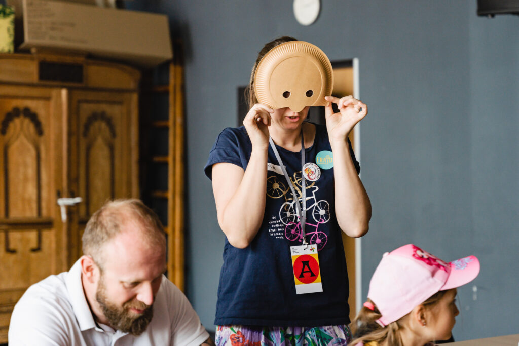 Kobieta przykłada sobie do twarzy papierowy talerzyk z wyciętymi otworami na oczy.