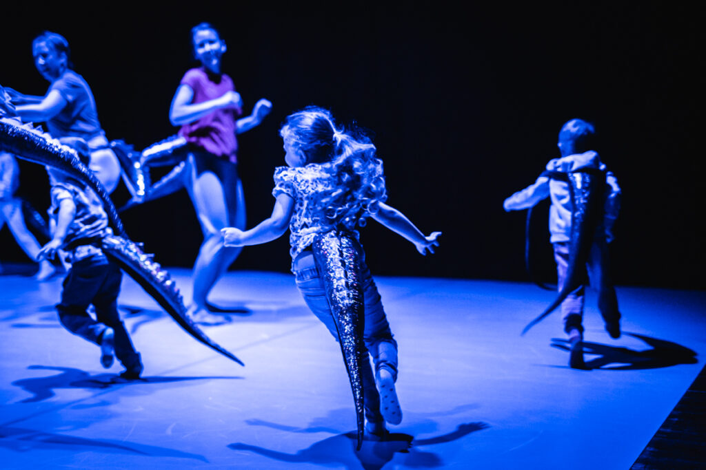 Po scenie biega grupa dzieci z przywiązanymi długimi ogonami.