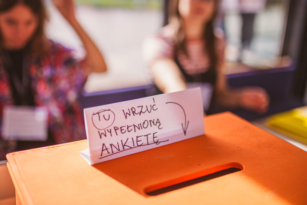 drewniana skrzynka z otworem do wrzucania głosów z napisem tu wrzuć wypełnioną ankietę