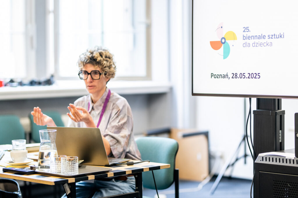 Nikola Schellmann przy biurku, mówi do publiczności