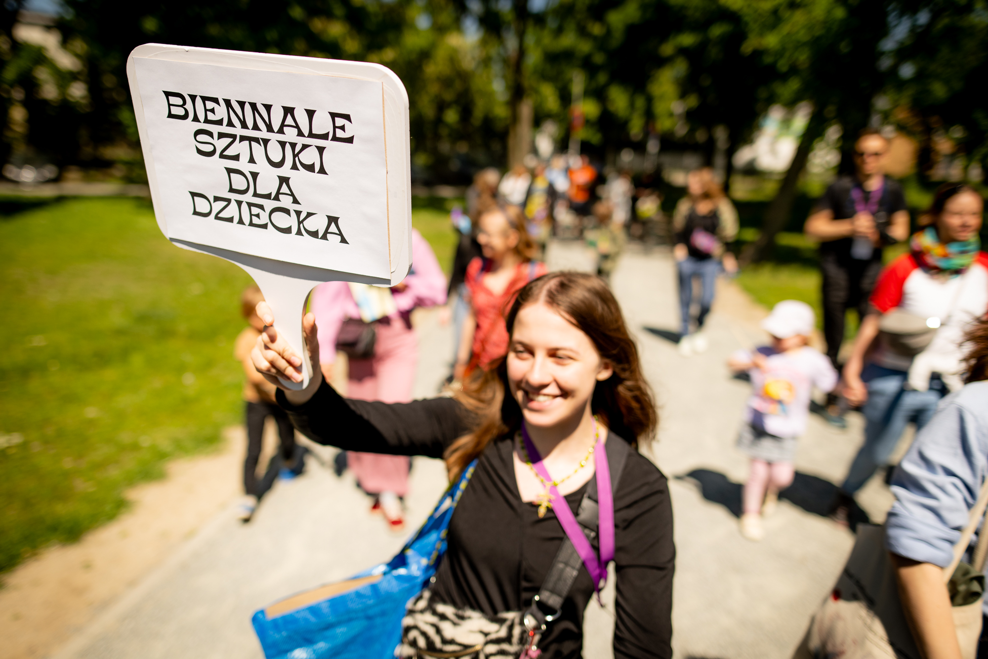 kobieta idzie przed grupą z transparentem z napisem Biennale Sztuki dla Dziecka